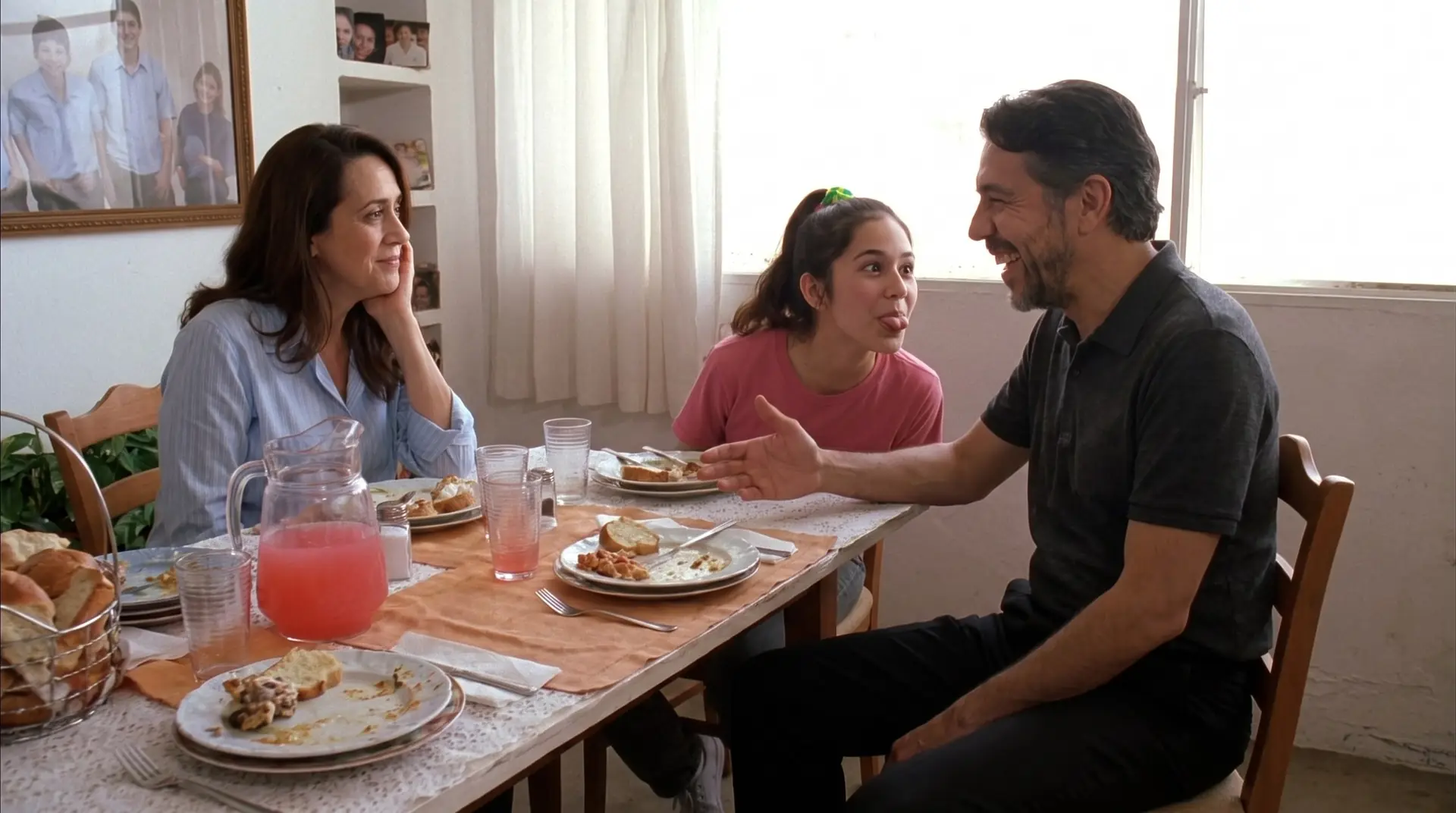 Familia comiendo junta en casa: el papá ríe, la hija adolescente hace una payasada y la mamá lo mira con cariño